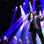 George Michael Impersonator singing with 3 female backing singers in sparkly dresses, a male backing singer also dressed in black and a keyboardist