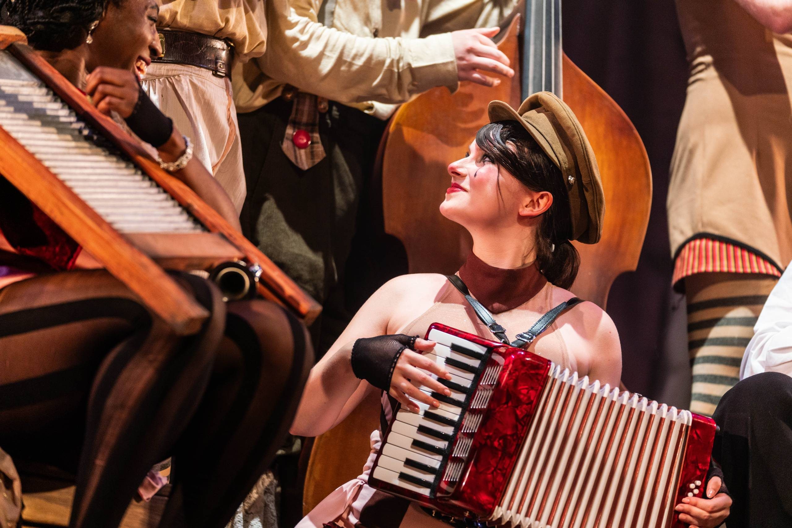 A female character wearing face makeup, and a soldiers hat plays an accordion.