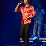 Black man with afro and beard in red open-necked shirt singing