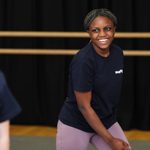 a young pariticpant wearing a navy blue Mayflower branded top and violet leggings is smiling.