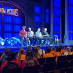 4 white men from Singin' in the Rain are sat on stools on the stage taking questions from a young audience.