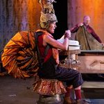 a female sits on a homemade trolley with another homemade contraption on her head.