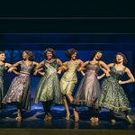 Tina linking arms with five black laughing women in dark dresses.