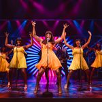 Tina and four black backing singers in yellow dresses throwing their hands in the air.