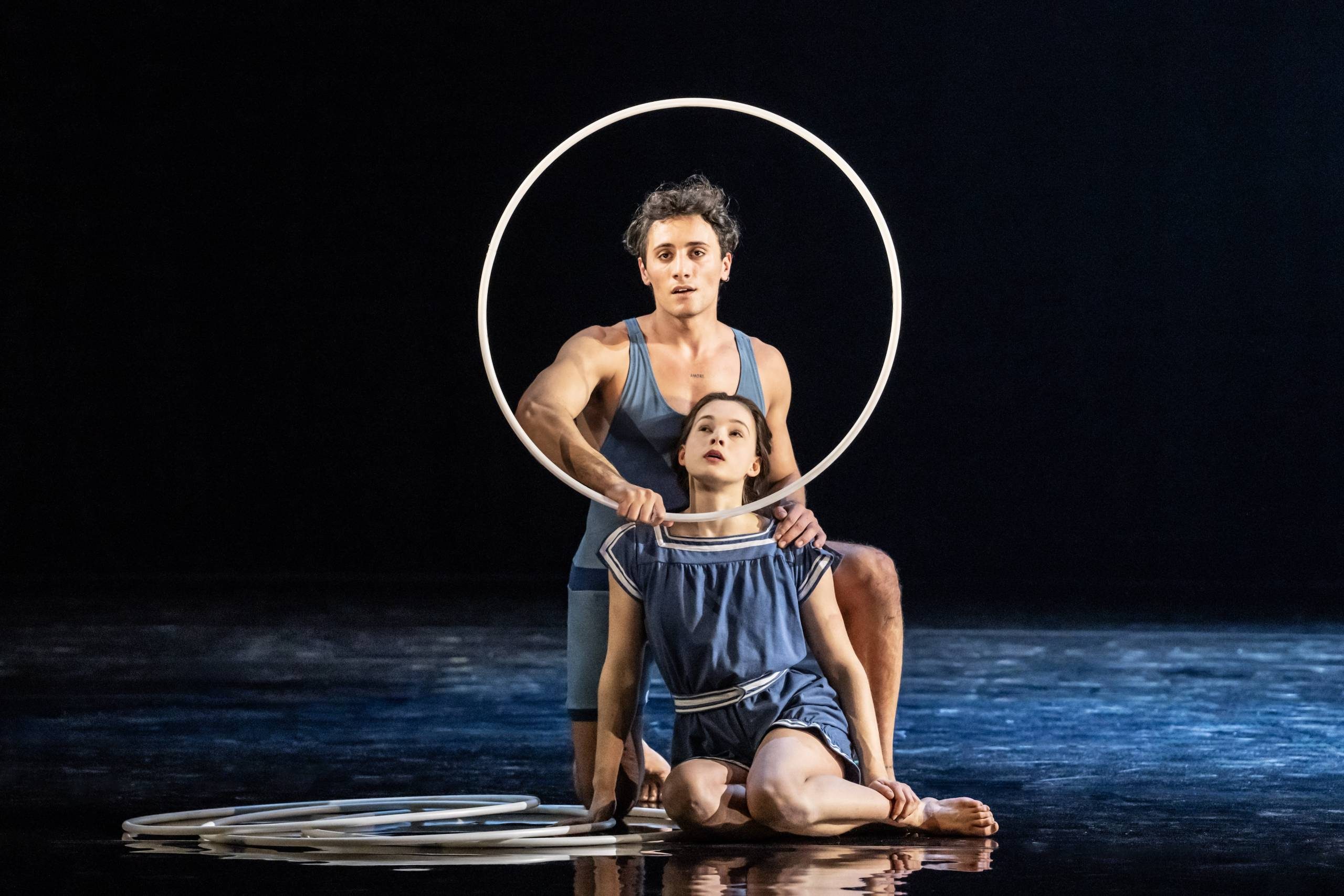 Saggese Jaschiu (Riccardo Frederico) holds a hoop vertically around Daughter's (Selma Hellmann) head.