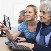 Several students sitting in pairs with elderly people, working together at computers.