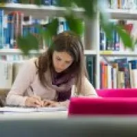 A female student studying various texts at a desk in the library