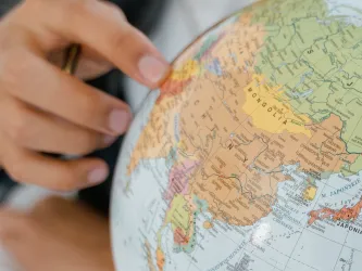 The hand of a young person points to a country on a globe model